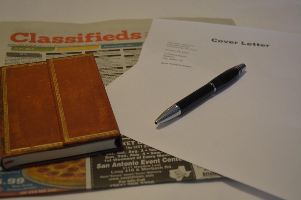 Close-up of a cover letter and pen placed on top of a newspaper classifieds section, with a small leather notebook beside them, representing a job search or career application process.  Image by Trudi Nichols from Pixabay